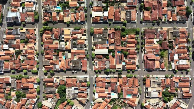 Aerial view of a dense residential neighborhood with terracotta tiled roofs and green trees lining the streets