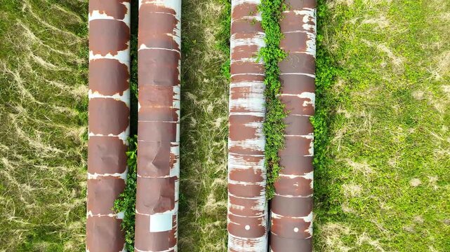 Aerial view of industrial pipes for gas, water, and oil running parallel across a green landscape, showcasing their weathered surfaces and surrounding vegetation in a natural setting