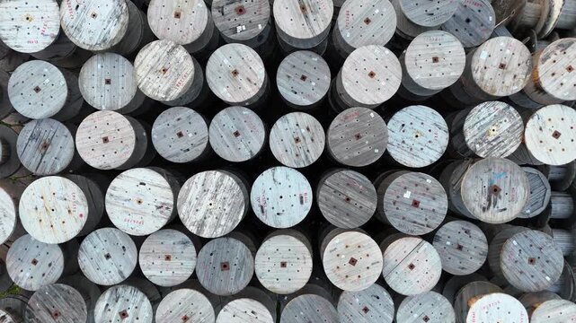 Aerial view of numerous wooden cable spools stacked closely together, showcasing their circular shapes and varied textures in a well-organized outdoor storage area