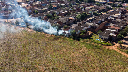Obraz premium Aerial view of smoke rising from a field adjacent to a residential neighborhood with dense housing and tiled roofs