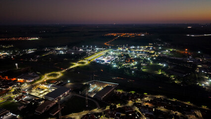 Obraz premium Aerial drone view of a sprawling industrial complex and residential area at dusk with illuminated streets and buildings