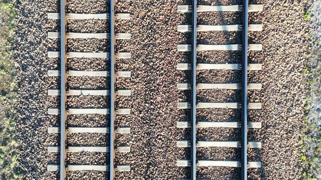Top view of railway tracks showing continuous progression of rails and sleepers, with gravel and sunlight creating distinct patterns across the surface