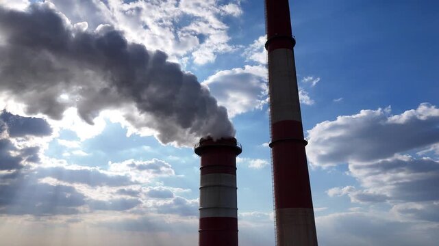 Industrial smokestacks emit white smoke against a bright sky, with sunlight filtering through clouds, highlighting the connection between energy production and environmental effects