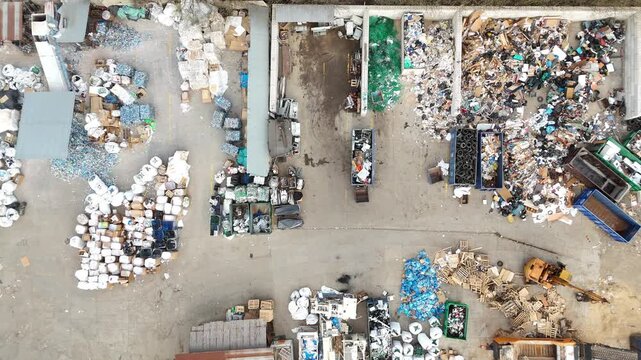 Aerial view of waste sorting and recycling process showing piles of garbage, containers, and vehicles in a waste management facility, highlighting the organization of recyclable materials