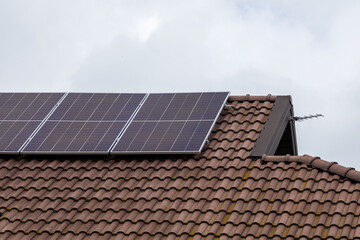 Fototapeta premium Solar Panels Harnessing Energy on a Tiled Roof of a Modern House Surrounded by Soft Clouds Under a Bright Sky
