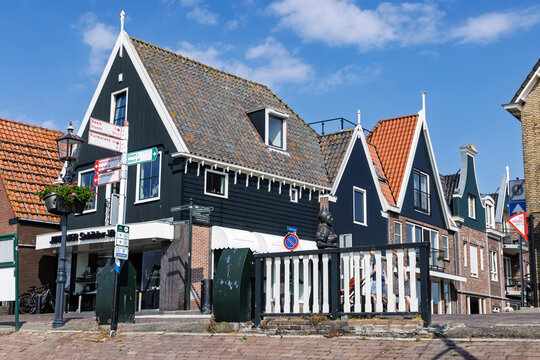 Volendam, Netherlands - May 31, 2026: Historic street corner with a directional signpost, statue in traditional dress, and classic gabled houses.
