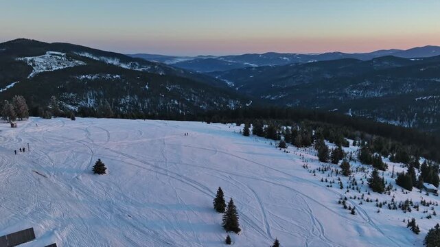 Aerial pull back tracking hikers silhouettes walking on snow covered mountain slope in first morning rays