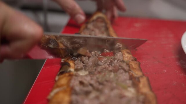 Professional chef cutting a freshly baked Turkish pide on a red cutting board in a restaurant, fa01