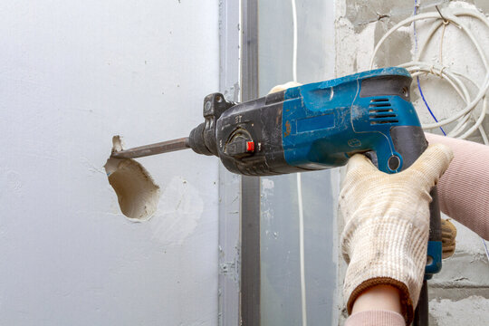 Builder uses electric hammer drill to break concrete wall. Worker renovates room during house construction. Professional repair service, building maintenance and renovation concept