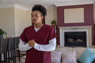 Obraz premium Man in maroon scrubs standing with clasped hands in living room near sofa, fireplace