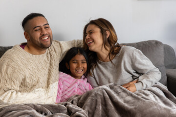 Parents with child sitting on gray couch at home sharing plush blanket while wearing pink robe © wavebreak3
