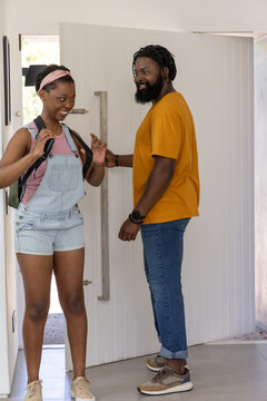 African father and teen in overalls standing in entryway holding metal pull and adjusting backpack