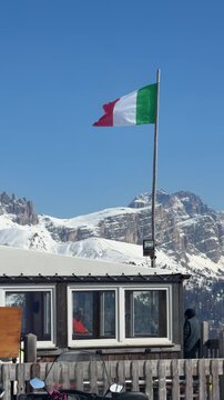 Mountain refuge in the Dolomites, Italy, with the Italian flag and spectacular snow-covered peaks. Alpine travel, ski tourism and outdoor adventure in the Dolomiti Superski region