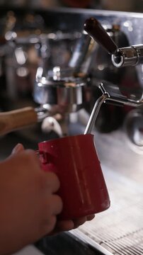 Close-up of a barista steaming and frothing milk using a professional espresso machine. Coffee preparation process in a cafe, creating microfoam for latte art and specialty coffee drinks