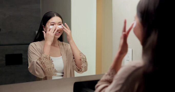Mirror, beauty and asian woman with eye patches in bathroom for collagen treatment in home. Female person, skincare mask or cosmetics with facial for hydration, vitamin C or hyaluronic acid in house