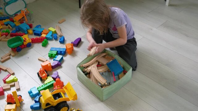 Child puts the toys in the box to establish order. Kid 5 years old establish order. Caucasian little girl tidying. The toddler baby himself cleans up, collects toys in the nursery after game playing.