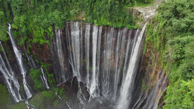 Drone view of Tumpak Sewu Waterfall cascading through a steep canyon surrounded by dense tropical vegetation in East Java, Indonesia.