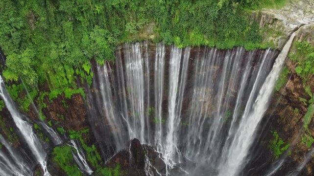 Drone view of Tumpak Sewu Waterfall cascading through a steep canyon surrounded by dense tropical vegetation in East Java, Indonesia.