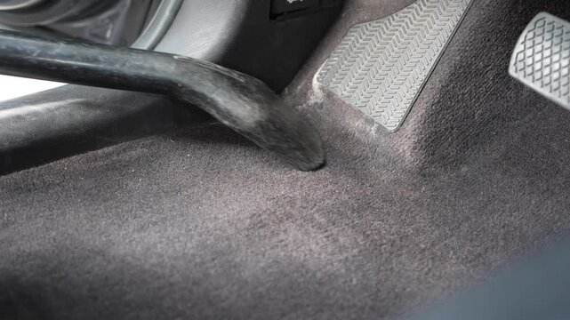 Close-up shot of a man cleaning the driver side carpet floorboard and footwell near the pedals with a vacuum cleaner nozzle. Hands-on automotive interior detailing, vehicle maintenance, family concept