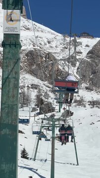 Skiers riding a chairlift above snowy slopes in Colle Santa Lucia, Dolomites. Scenic ascent through the Dolomiti Superski area surrounded by dramatic alpine peaks and winter landscapes