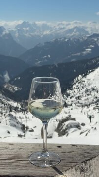 Glass of Prosecco overlooking the snowy Dolomites near Cortina d'Ampezzo, Italy. Relaxing alpine lifestyle, slow living atmosphere and panoramic mountain views in Dolomiti Superski