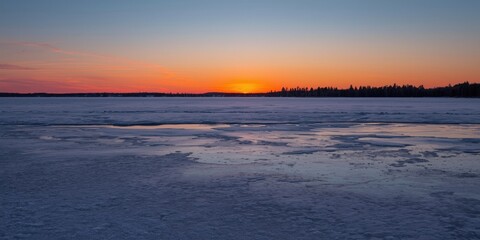 Obraz premium ice covered pond alongside a vivid sunset horizon