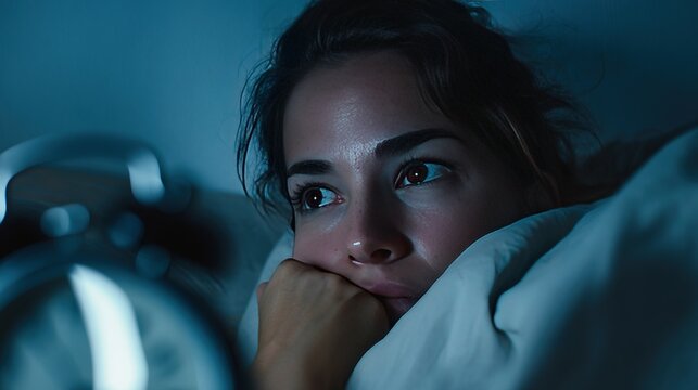 Closeup portrait of sleepless anxious woman lying in bed under blanket, dark blue dim bedroom night lighting, insomnia mental health concept