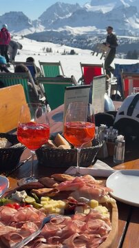 Traditional Italian aperitivo with Aperol Spritz, cured meats and cheese served on a sunny mountain terrace at Dolomiti Superski, Italy. Apr&egrave;s-ski dining experience with panoramic snowy slopes, alpine