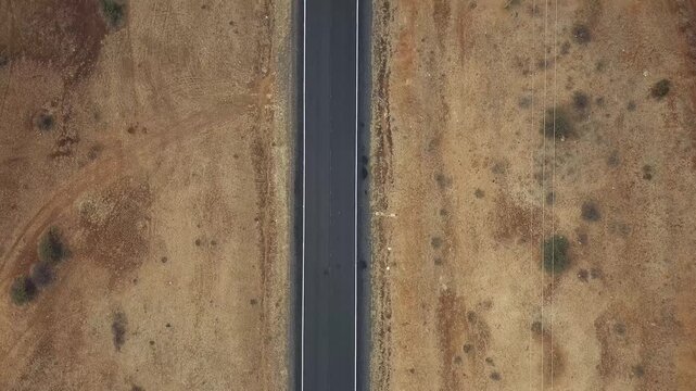 Aerial top-down drone shot of straight empty paved road cutting through dry African savanna bushland