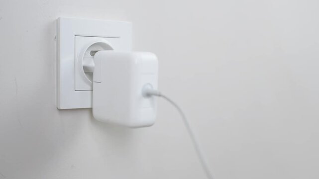 Male Hand Plugging Charger Into White Electrical Wall Socket