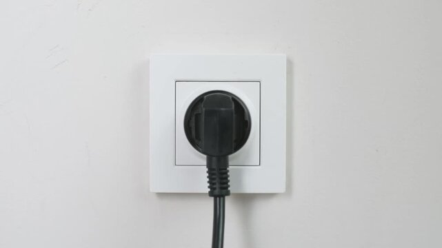 Male Hand Plugging Charger Cable Into White Wall Socket
