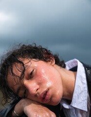 Fototapeta premium Young Person with Wavy Hair Posing Under Cloudy Sky in Rainy Weather with Dramatic Expression