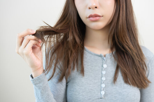 Damaged Hair, frustrated asian young woman, girl hand in holding splitting ends, messy unbrushed dry hair with face upset, long disheveled hair, health care of beauty. Portrait isolated on background