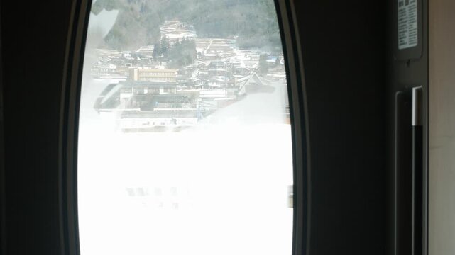 view through window on dtrain's door outside bullet highspeed train while travel through japan countryside with view of small city full with white snow in daytime,view outside train while moving fast