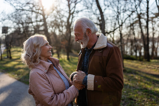Happy senior couple holding hands and sharing an affectionate moment in a park. Warm lifestyle portrait symbolizing lasting love, emotional connection, trust, and companionship