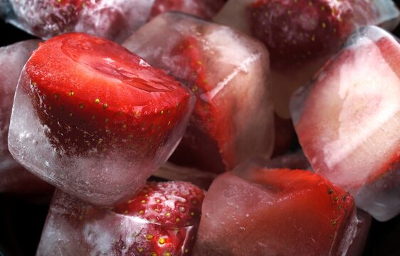 Frozen strawberries in ice cubes with melting water and reflections