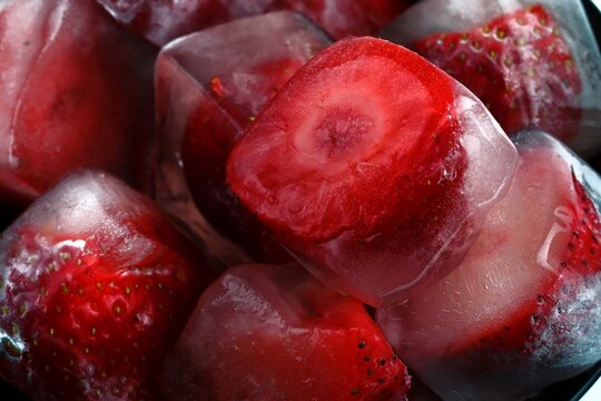 Frozen strawberries in ice cubes with melting water and reflections