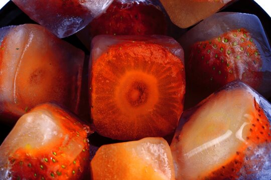 Frozen strawberries in ice cubes with melting water and reflections