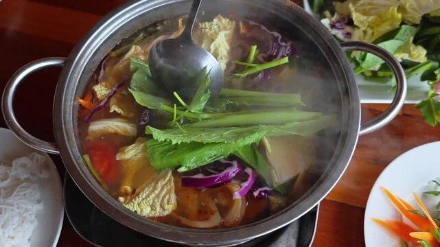Cooking soup. Seafood and vegetables hot pot served in Asian restaurant. Vietnamese Hot pot cuisine. Steming hot pot over flame at Asian restaurant table. 