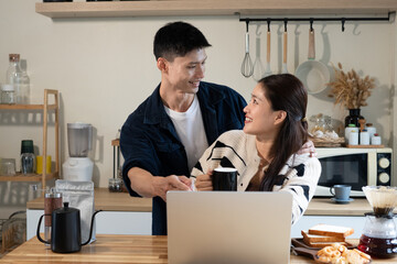Fototapeta premium Happy Asian Couple Smiling Together in Modern Kitchen with Laptop and Coffee in the Morning