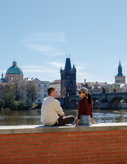 Naklejka premium A couple sits peacefully by the Vltava River, enjoying a sunny day in Prague, Czechia