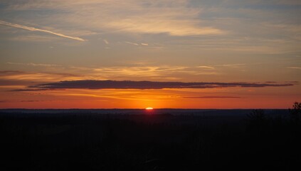Fototapeta premium Sunset horizon painted with drifting clouds above natural woodland