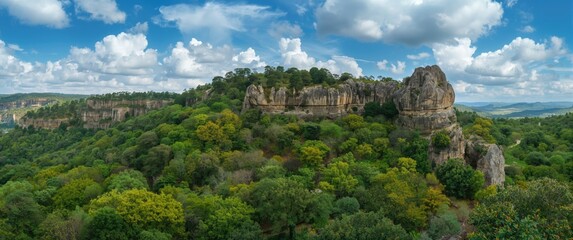 Obraz premium Top down view of a thriving green hillside with dense tree clusters near craggy rock cliffs and pristine sky