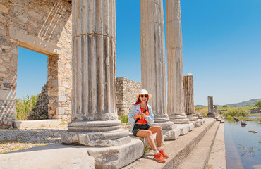 Naklejka premium Woman tourist sitting among ancient Roman columns and ruins in Miletus, exploring history and landmark architecture