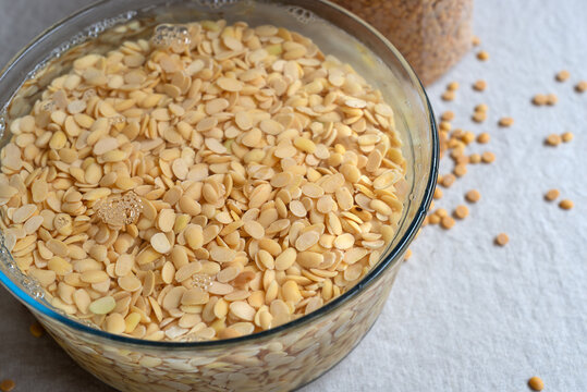 Yellow split soybeans soaking in water inside a glass bowl.