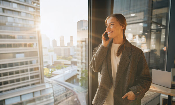 Confident young Caucasian female entrepreneur smiling during a phone call in warm golden hour light with an optimistic business vibe