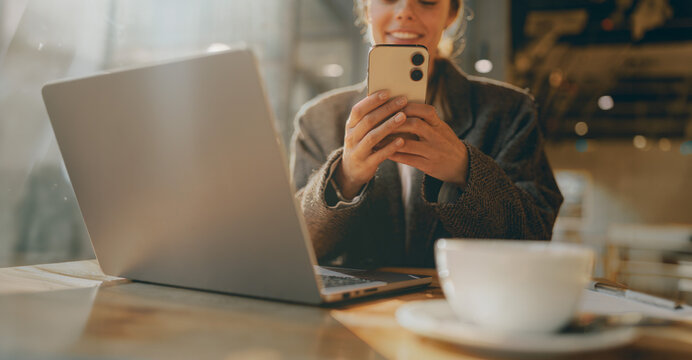 Smiling Caucasian young woman holding her phone in a cozy cafe with warm natural light creating an authentic and relaxed freelance vibe