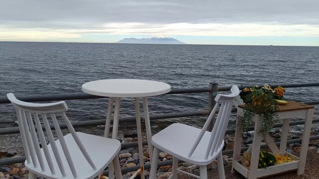 Empty white table and chairs on the seashore with a view of the island of Samothrace in Greece, eb01