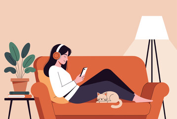 Fototapeta premium Cozy scene of a woman relaxing on a living room sofa with her cat while listening to music and using her smartphone for entertainment.