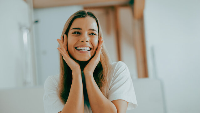 A cheerful Caucasian woman enjoys her morning skincare routine in soft natural indoor light with a clean authentic wellness vibe